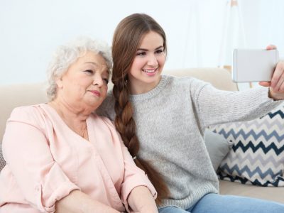 Beautiful girl with grandmother taking selfie on couch at home